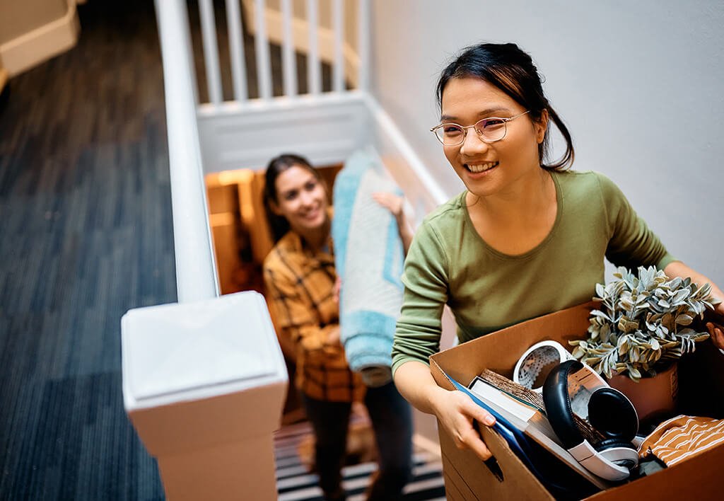 Move in Tips - An Asian & Middle Eastern Woman Smiling Carrying Boxes up Narrow Apartment Stairs